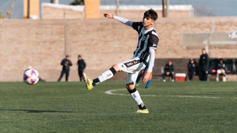 Teenage soccer player kicking a ball during a match on an outdoor field.