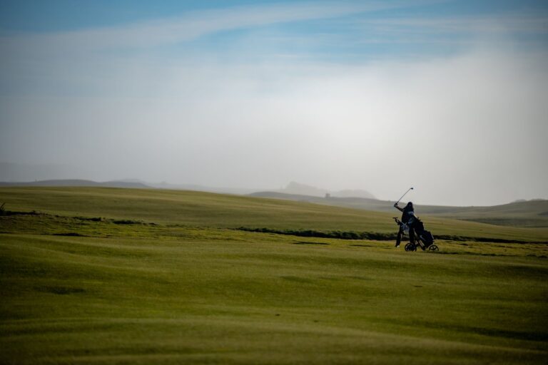 A golfer swings on a vast, misty course under a clear sky, illustrating serene sportsmanship.