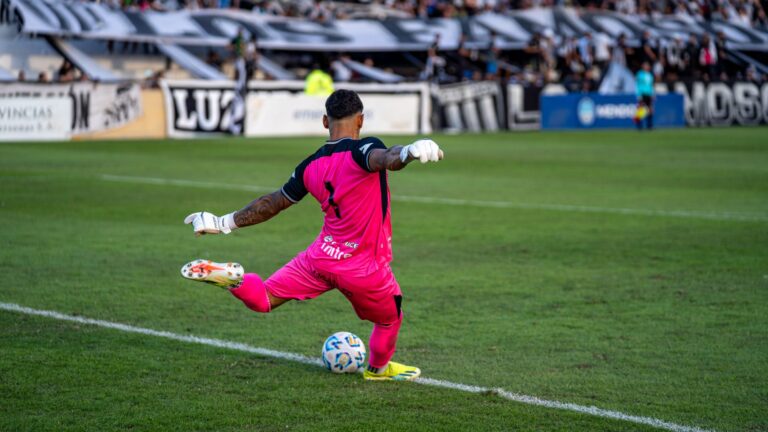 Goalkeeper in pink kit kicking the ball during a soccer match.