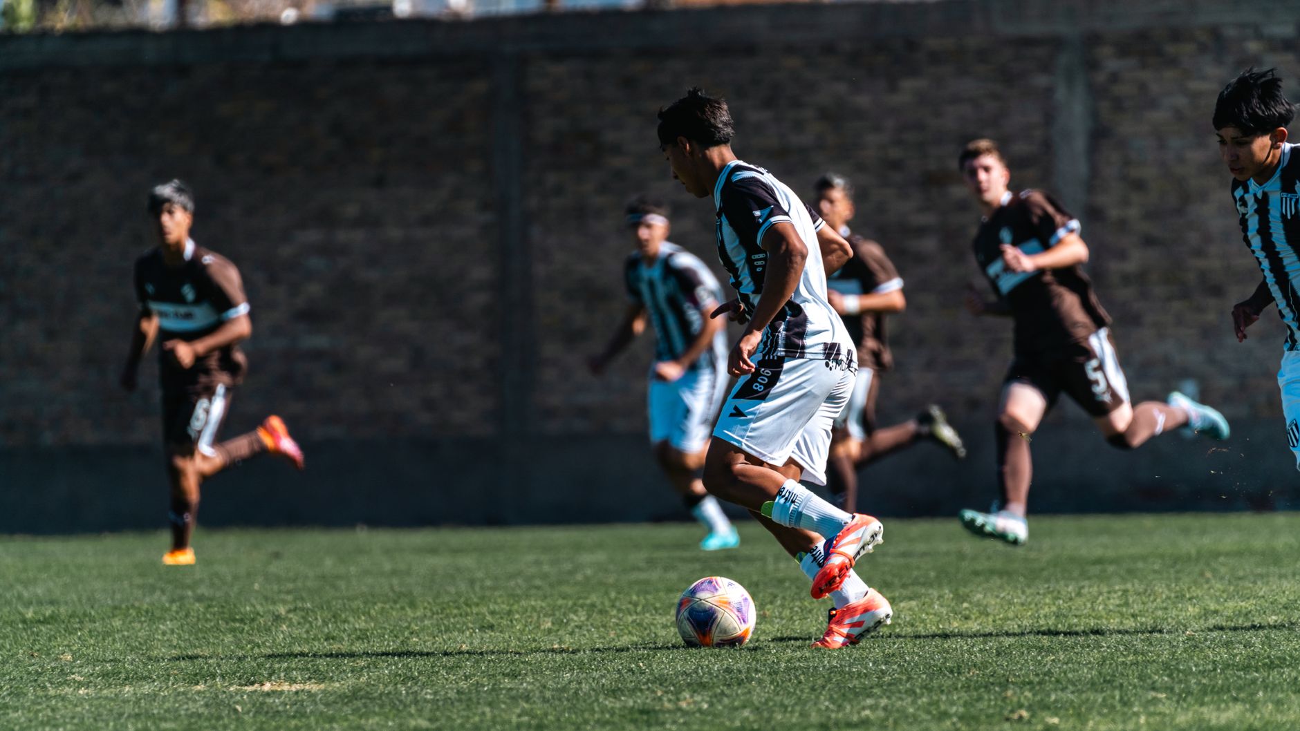 Dynamic soccer match with players running toward the goal on a sunny day.