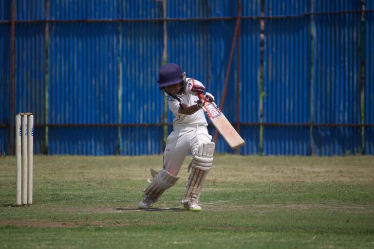 A young cricketer in action on a sunny day, playing on a grass field with a bat and wicket.