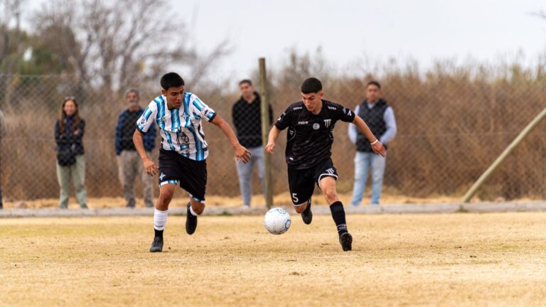 Two young male soccer players competing in a match outdoors on a grassy field.