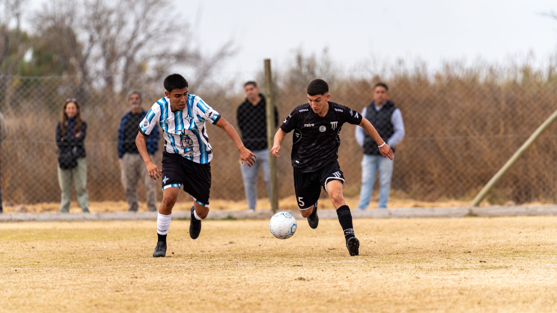 Two young male soccer players competing in a match outdoors on a grassy field.