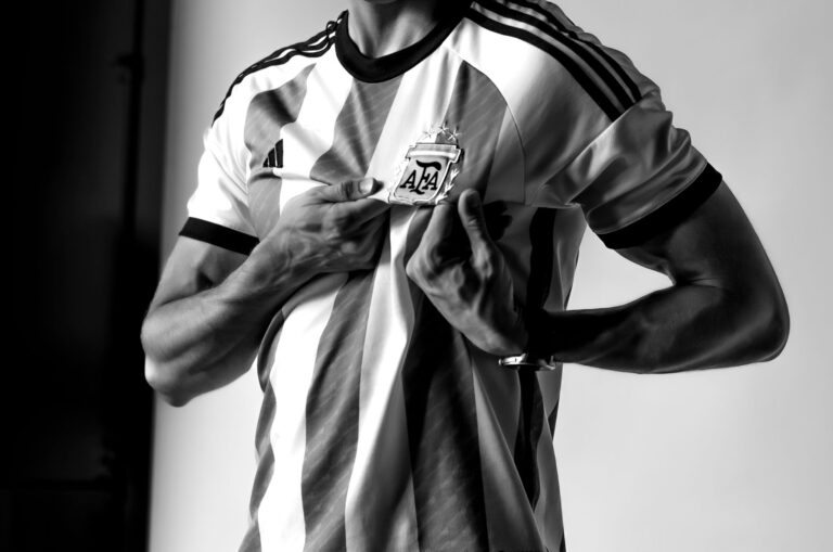 Black and white photo of a man holding the Argentine football crest on his jersey with pride.