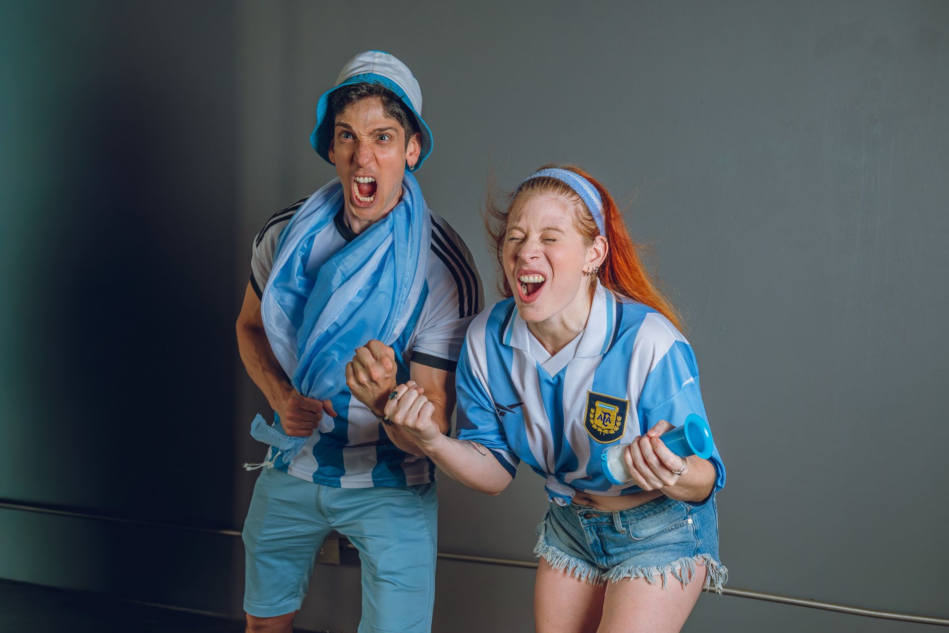Excited Argentinian fans celebrating a soccer game indoors, wearing team jerseys.
