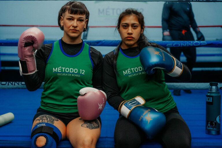 Two female boxers in Buenos Aires gym wearing gloves and green shirts in a boxing ring.