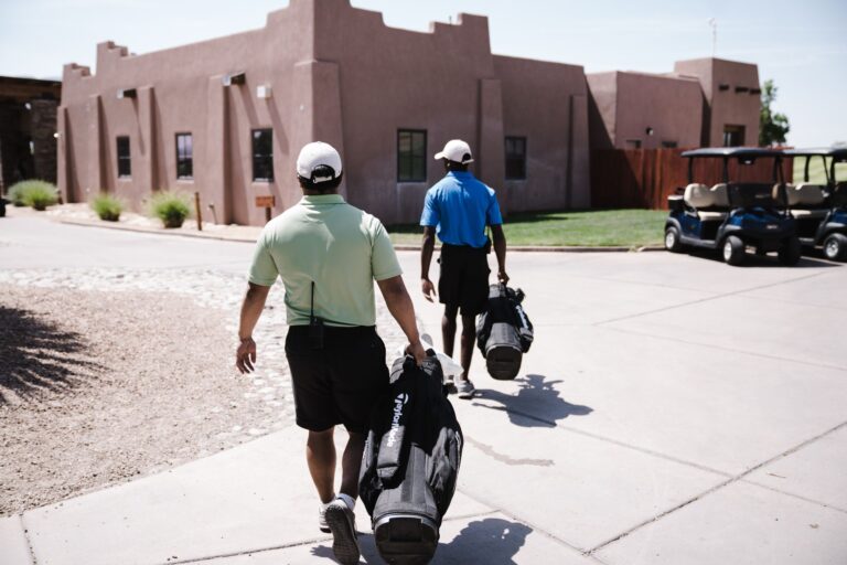Two golfers walking towards a golf cart carrying bags on a sunny day.