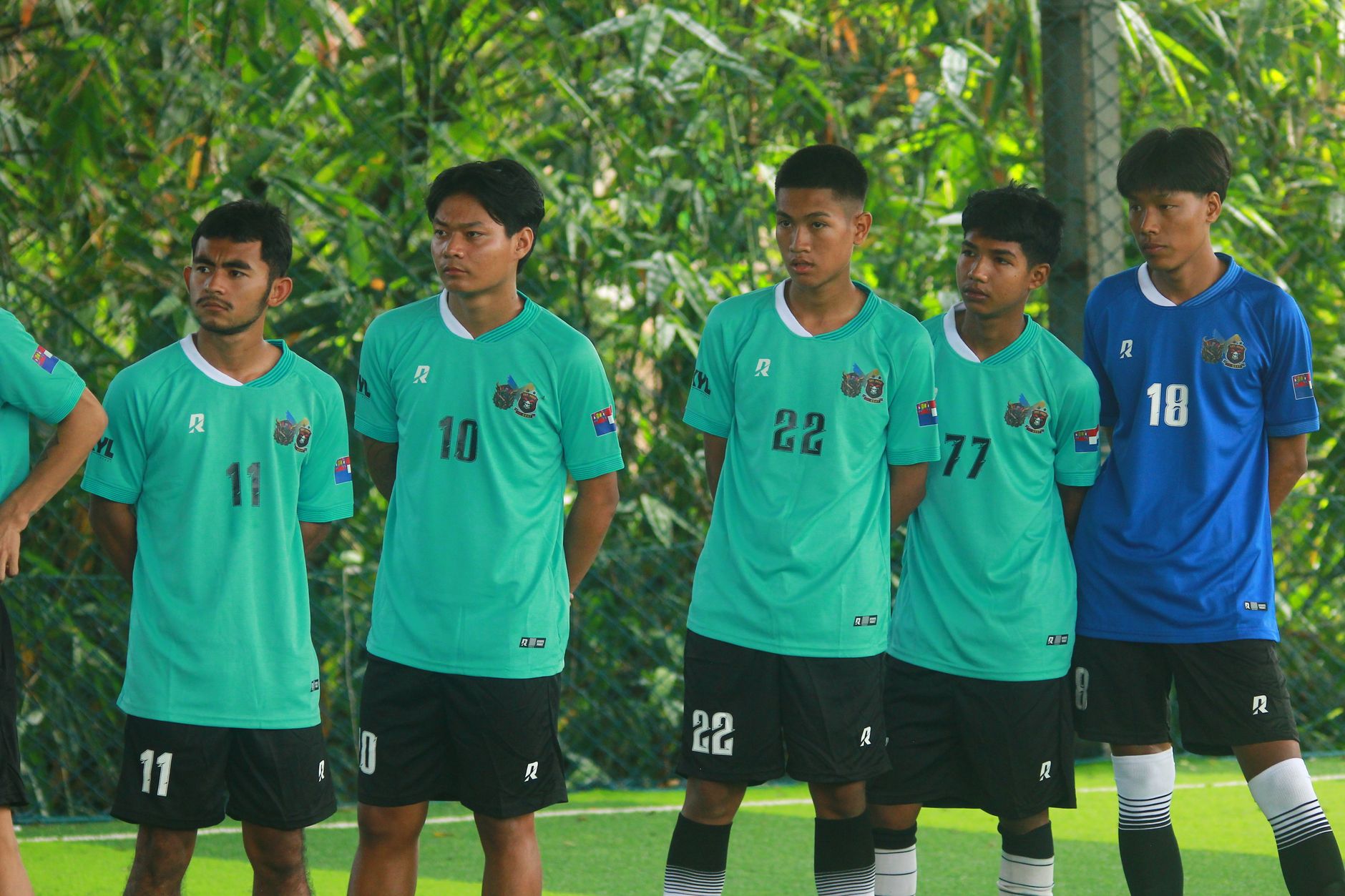 A group of young male soccer players in green jerseys standing outdoors in Myanmar.