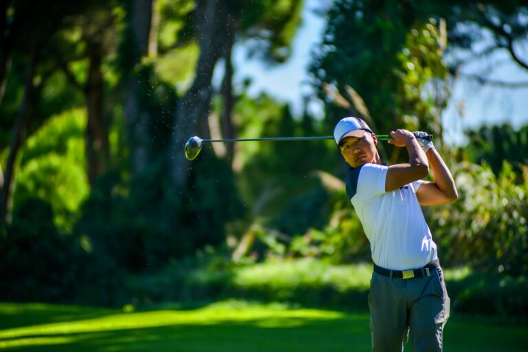 Asian golfer executing a powerful swing on a vibrant green golf course on a sunny day.