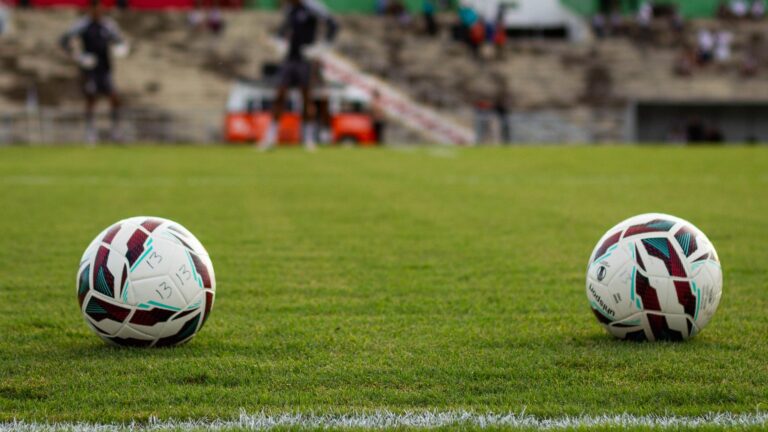 Two soccer balls resting on a vibrant green football field before a match begins.