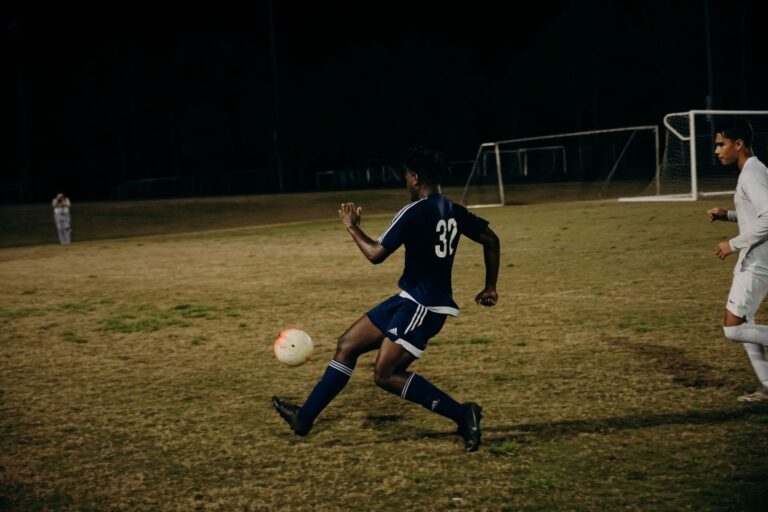Two players compete fiercely during a nighttime football match on a grass field.