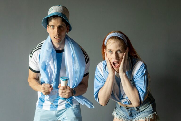 Two passionate Argentine fans celebrating with excitement, wearing team colors indoors.