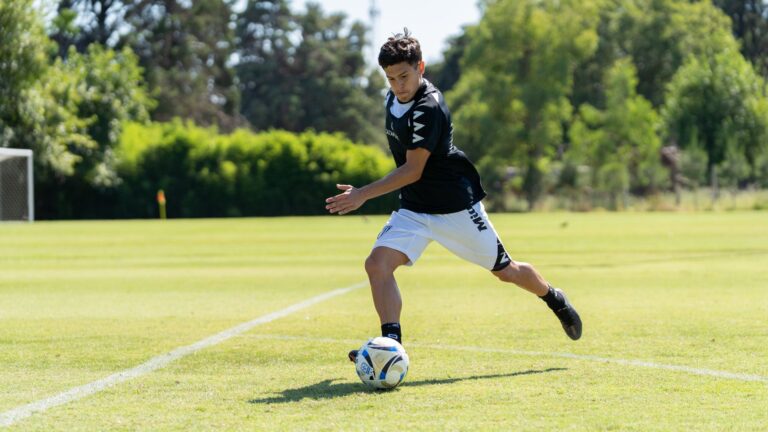 A teenager playing soccer on a sunny day, dribbling the ball on a grassy field.