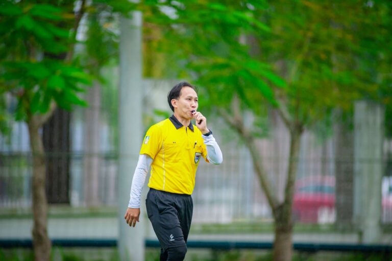 A referee in a yellow shirt blows a whistle during a soccer match in Hanoi, Vietnam.