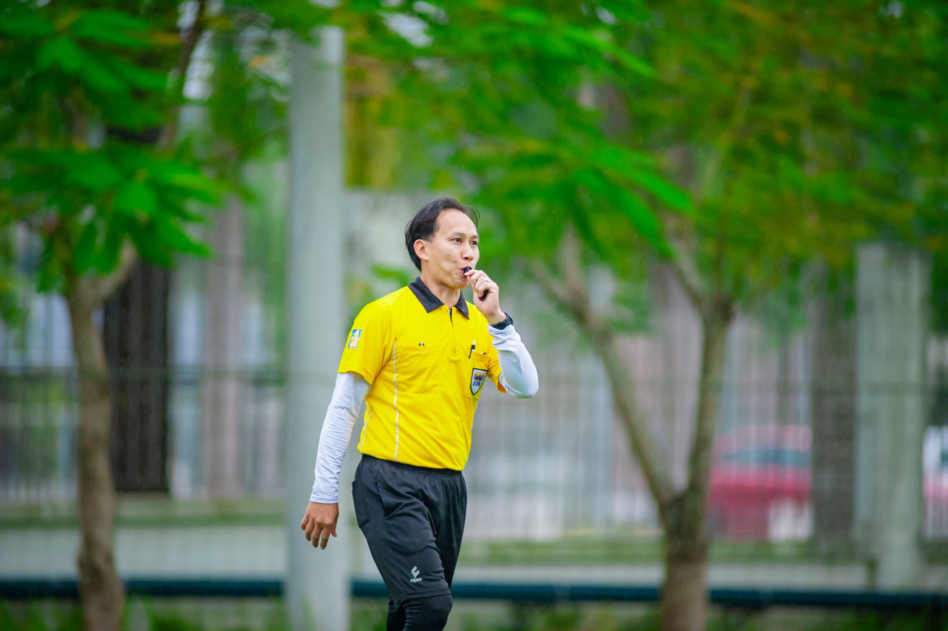 A referee in a yellow shirt blows a whistle during a soccer match in Hanoi, Vietnam.
