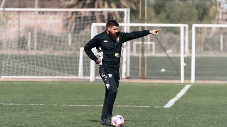 A soccer coach giving instructions during a practice session on an outdoor field.