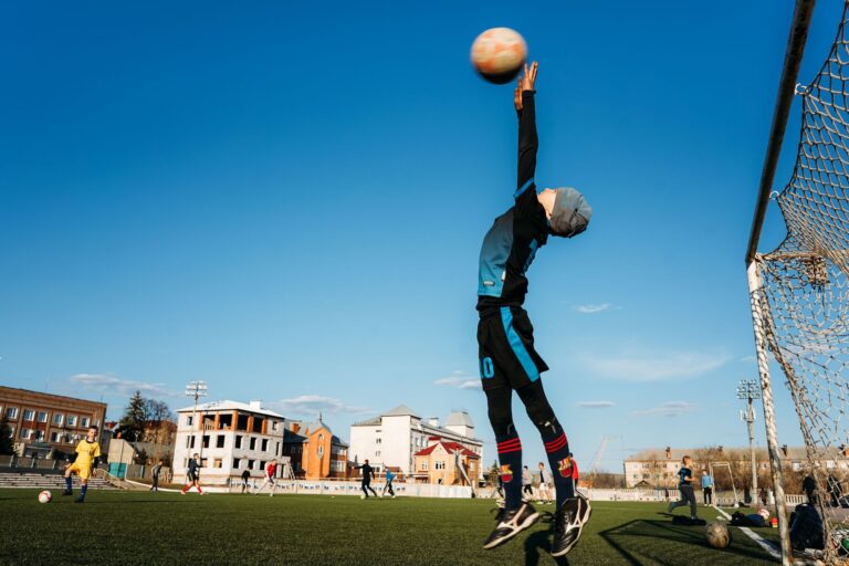 A child soccer player leaps to block a goal during an outdoor match on a sunny day.