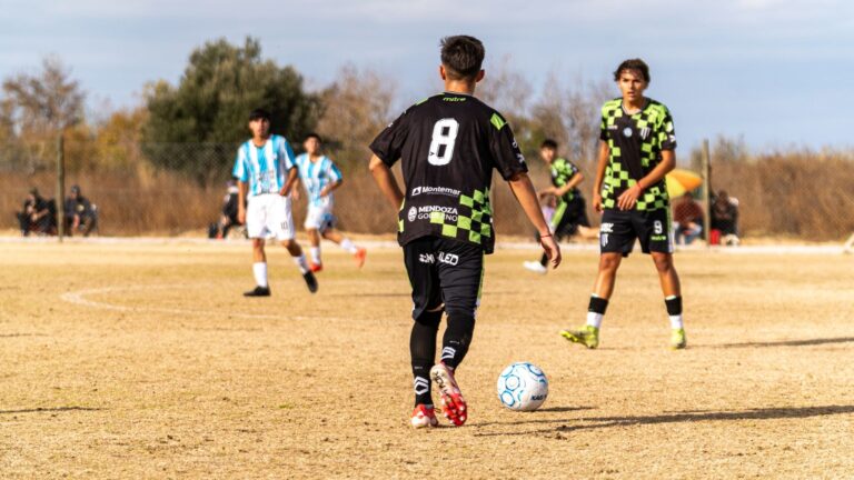 Boys playing soccer outdoors on a sunny day in team uniforms.