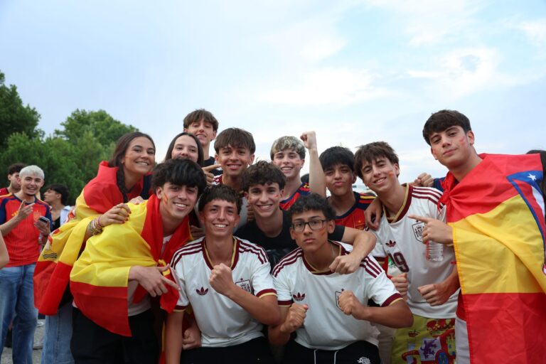 A cheerful group of young people celebrates outdoors, proudly displaying Spanish flags and team jerseys.