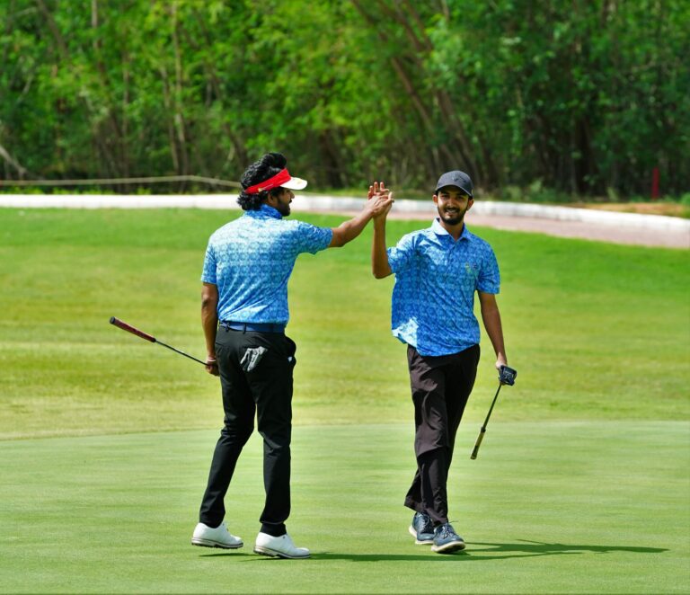 Two men on a golf course in Hyderabad high-fiving after a successful play.