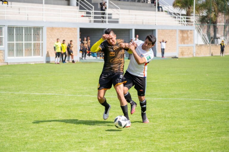 Two soccer players in action during a match on a sunny day in Texcoco, Mexico.