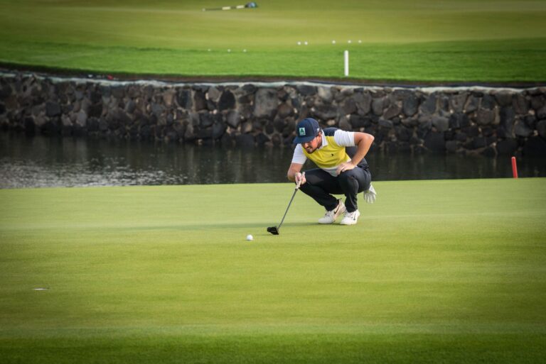 Golfer crouches to line up a putt on a sunny golf course morning.