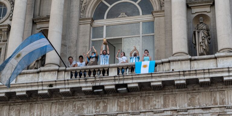 People celebrating with flags and a trophy on a Buenos Aires balcony.