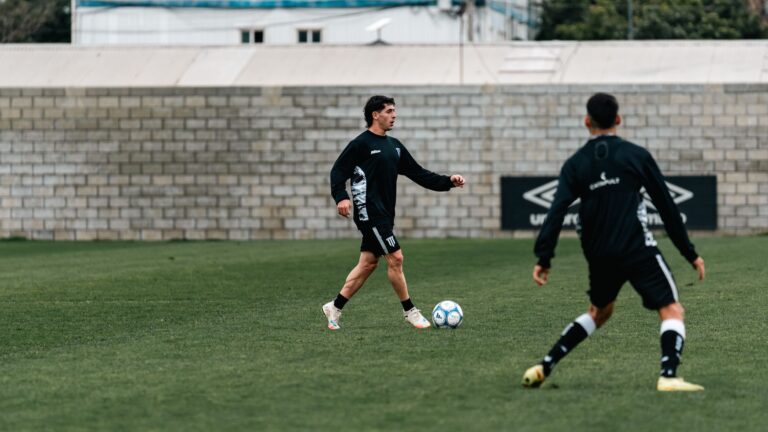 Two soccer players in black sportswear practicing on a green field, focusing on passing techniques.