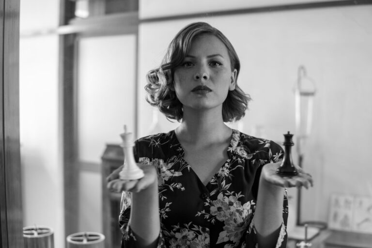 Black and white portrait of a woman holding chess pieces, symbolizing strategy and balance.