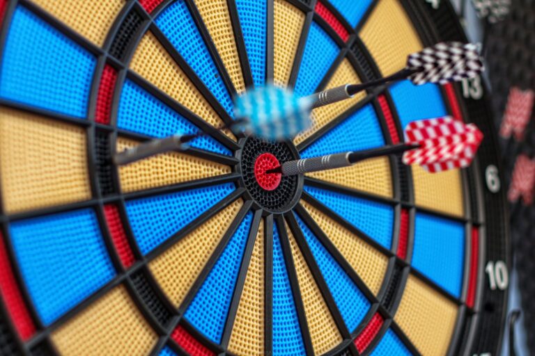 Colorful darts hit bullseye on dartboard, capturing precision and focus.