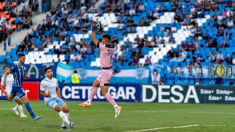Dramatic action shot of a goalkeeper catching the ball during a competitive soccer match on a bright day.