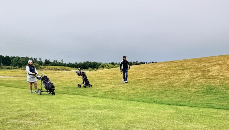 Two golfers on a lush green course in Skåne, Sweden, enjoying a leisurely game under a cloudy sky.