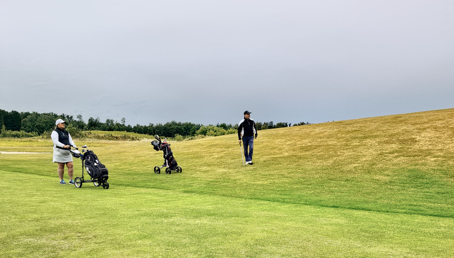 Two golfers on a lush green course in Skåne, Sweden, enjoying a leisurely game under a cloudy sky.