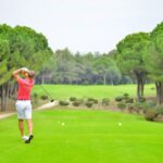 Back view of a golfer swinging a club on a lush golf course in Antalya, Türkiye.