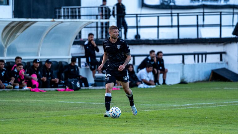 Soccer player dribbling during a match with team watching from the sidelines.
