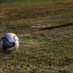 A lone soccer ball resting on a grassy field under sunlight.