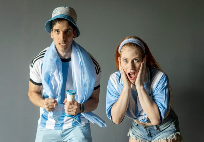 Two passionate Argentine fans celebrating with excitement, wearing team colors indoors.