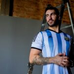 Adult male wearing an Argentina soccer jersey stands confidently indoors.