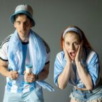 Two passionate Argentine fans celebrating with excitement, wearing team colors indoors.