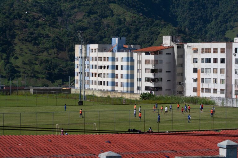 Aerial view of a youth soccer match in a Venezuelan residential area surrounded by lush greenery.