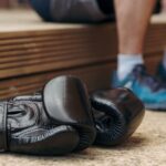 Black boxing gloves resting on floor with athlete in background. Ideal for sports and fitness themes.