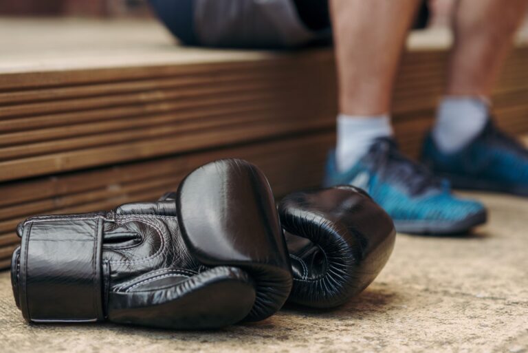 Black boxing gloves resting on floor with athlete in background. Ideal for sports and fitness themes.
