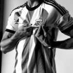 Black and white photo of a man holding the Argentine football crest on his jersey with pride.