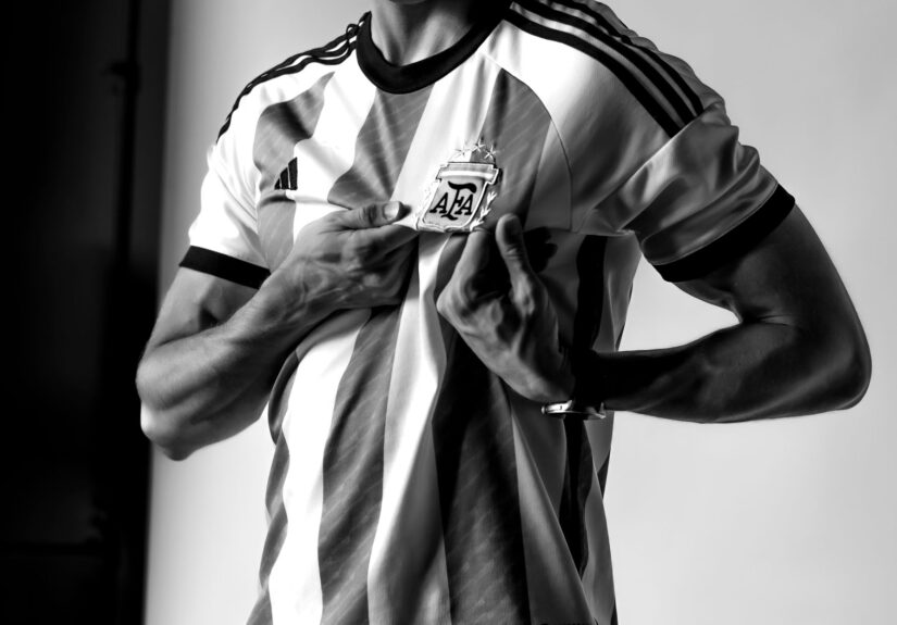 Black and white photo of a man holding the Argentine football crest on his jersey with pride.