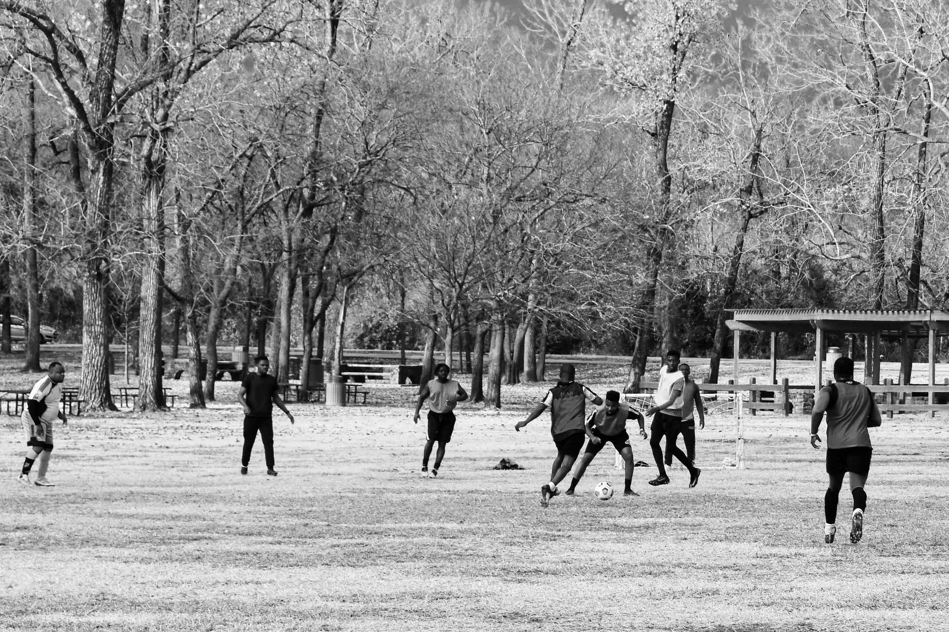 A group of men playing soccer in a park in Arlington, Texas, captured in black and white.
