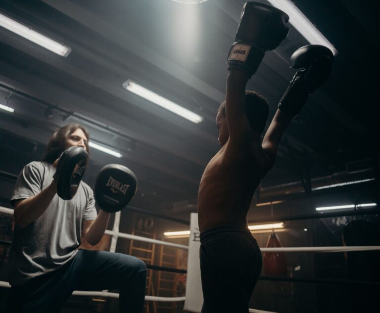 Child boxer triumphantly raises arms during boxing training session indoors.
