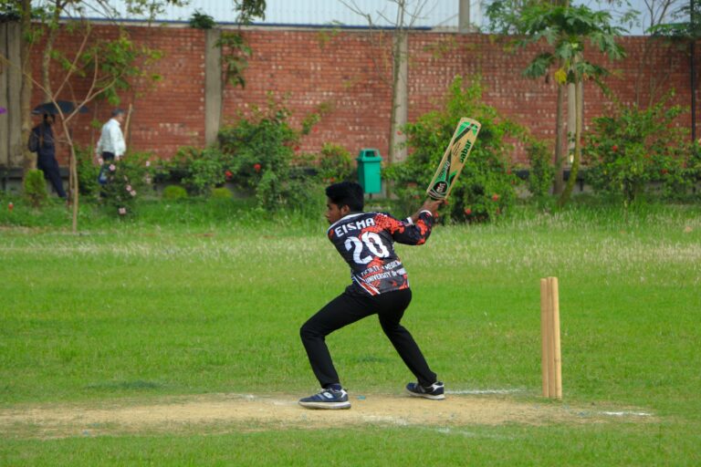 A young male cricketer takes a swing at the ball during a cricket match on a sunny day.