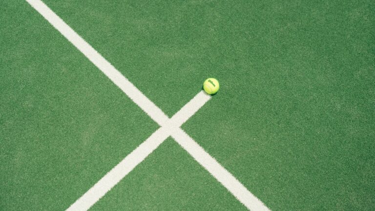 A bright green tennis ball on a green tennis court with white lines in Miami, FL.