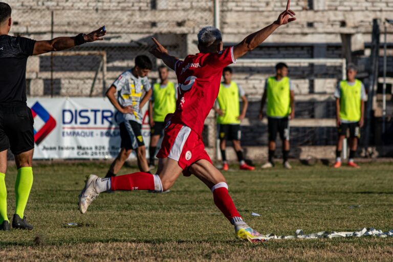 A soccer player in red celebrates a goal with enthusiasm on an outdoor field.