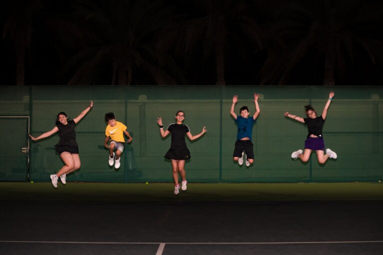 Group of teenagers jumping in celebration on an outdoor tennis court at night.
